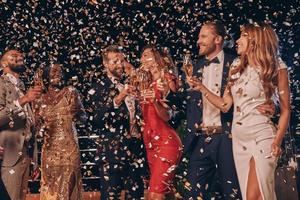 Group of beautiful people in formalwear having fun together with confetti flying all around photo