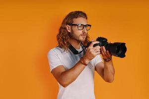 un joven apuesto con ropa informal usando una cámara fotográfica mientras se enfrenta a un fondo amarillo foto