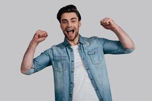 Always winning. Handsome young man in casual wear gesturing and looking at camera while standing against grey background photo