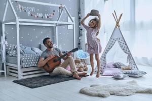 Feeling proud for his daughter. Young father looking at his little daughter and smiling while she jumping in bedroom photo