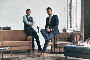 hombres con un gran estilo. dos jóvenes apuestos en trajes mirando a la cámara mientras descansan en el interior foto