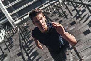 His best speed. Top view of young man in sports clothing running on the stairs while exercising outside photo