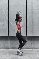 dispuesto a superar cualquier obstáculo. Longitud total de mujer joven moderna en ropa deportiva saltando la cuerda mientras hace ejercicio al aire libre foto