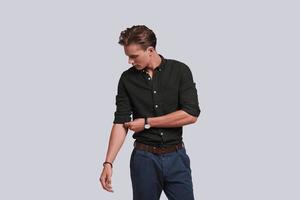 Used to look perfect. Good looking young man adjusting the sleeve of his shirt while standing against grey background photo