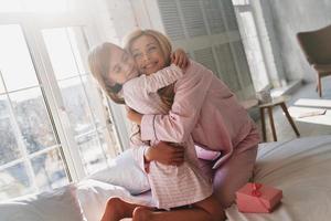 felices de estar juntos. linda niña abrazando a su madre mientras se sienta en la cama en casa foto