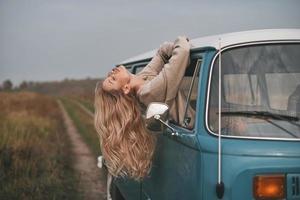 totalmente libre. Una joven atractiva que se asoma por la ventana de la furgoneta mientras disfruta del viaje en coche foto