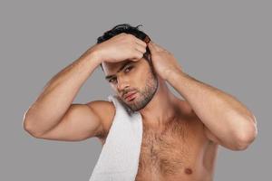 Perfect man. Good looking young man combing his hair while standing against grey background photo