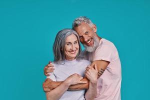 Romantic senior couple looking at camera and smiling while standing together against blue background photo