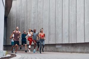 toda la longitud de los jóvenes en ropa deportiva trotando mientras hacen ejercicio al aire libre foto