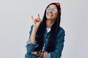 Attractive young woman in bandana gesturing and smiling while standing against grey background photo