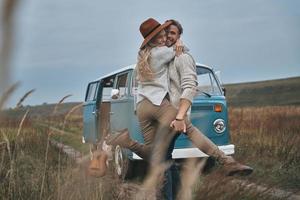 felicidad despreocupada. hermosa pareja joven abrazándose y sonriendo mientras está de pie cerca de la mini furgoneta de estilo retro azul foto