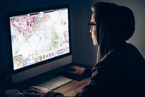 juego de noche vista lateral de un joven jugando videojuegos mientras está sentado en la mesa en una habitación oscura foto