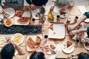 Delicious dinner. Close up top view of young people picking pizza while having a dinner party indoors photo