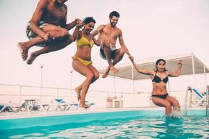 disfrutando juntos de la fiesta en la piscina. grupo de hermosos jóvenes que se ven felices mientras saltan juntos a la piscina foto