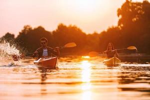 pareja en kayak juntos. Una pareja joven segura de sí misma haciendo kayak en el río junto con la puesta de sol en el fondo foto