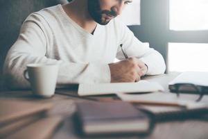 Making some important notes. Close-up of confident young man writing something in notebook while sitting at his working place in office photo