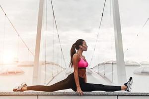 entrar en el ritmo del yoga. mujer joven moderna en ropa deportiva haciendo las divisiones mientras hace ejercicio al aire libre foto