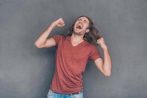 Everyday winner. Happy young man in casual wear standing against grey background and gesturing photo