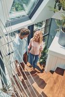 Beautiful mature couple examining new house while walking up by stairs together photo