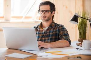 Modern technology for creative work. Confident young man working on laptop while sitting at his working place photo