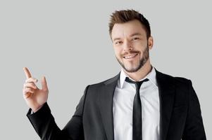 Businessman pointing copy space. Portrait of cheerful young man in formalwear pointing away and smiling while standing against grey background photo