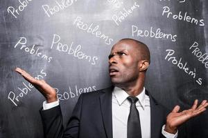 Problems all around me. Depressed African man in formalwear standing against blackboard with inscription Problems and gesturing photo