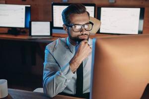Confident young man working on computer while staying late in the office photo