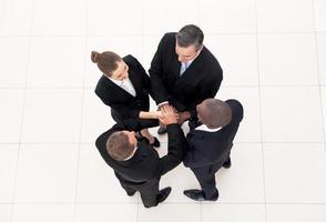 We are team. Top view of four business people in formalwear standing close to each other and holding hands together photo