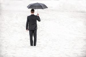 Safe business. Rear view of man in formalwear holding umbrella overhead while standing in desert photo