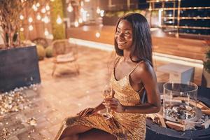 Beautiful young African woman in evening gown holding flute with champagne and smiling photo