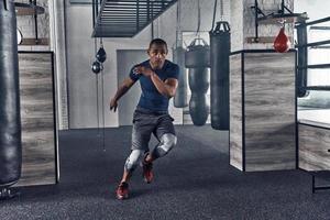 sigue moviéndote. toda la longitud de un apuesto joven africano con ropa deportiva corriendo mientras hace ejercicio en el gimnasio foto