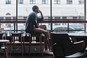 Enjoying nice day. Thoughtful young man looking outside while sitting in the cafeteria photo