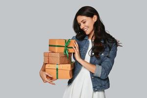 Christmas is coming... Attractive young woman smiling and carrying gift boxes while standing against grey background photo