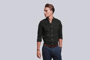 Confidence and charisma. Good looking young man keeping hand in pocket and looking away while standing against grey background photo