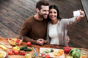 capturar momentos brillantes juntos. vista superior de una hermosa pareja joven haciendo selfie y sonriendo mientras preparan comida juntos foto