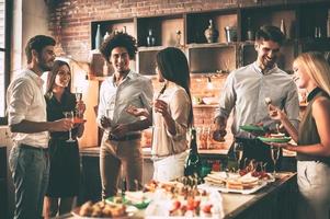 fiesta con los mejores amigos. grupo de jóvenes alegres que disfrutan de una fiesta en casa con bocadillos y bebidas mientras se comunican en la cocina foto