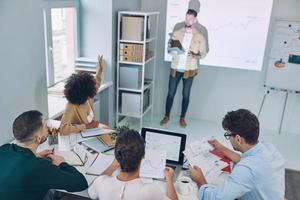 Group of young modern people in smart casual wear analyzing data on projection screen in the office photo