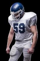 Feeling exhausted after game.  American football player looking down while standing against black background photo