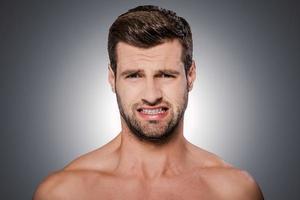 That is disgusting Portrait of frustrated young shirtless man looking at camera and grimacing while standing against grey background photo