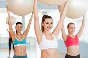 haciendo ejercicio con pelotas de fitness. tres hermosas mujeres jóvenes en ropa deportiva haciendo ejercicio con pelotas de fitness y sonriendo foto