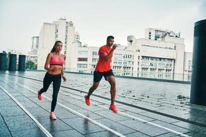 toda la longitud de un hombre y una mujer jóvenes con ropa deportiva saltando y trotando mientras hacen ejercicio en la calle de la ciudad al aire libre foto