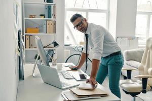 hombre de negocios moderno. apuesto joven mirando hacia otro lado y sonriendo mientras está de pie en la oficina foto