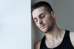 Feeling so badly. Depressed young man leaning at the wall and keeping eyes closed photo