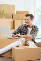 In search of a good design ideas. Handsome young man sitting on the floor and working on laptop while cardboard boxes laying in the background photo