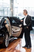 Examining car at dealership. Full length of confident mature man in formalwear opening the car door at the dealership photo