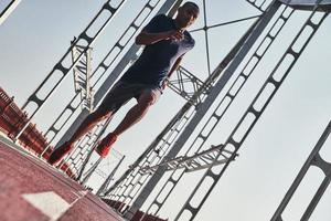 You can do it Full length of young African man in sports clothing exercising while jogging on the bridge outdoors photo