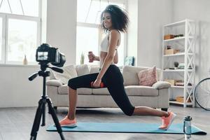 Attractive young African woman exercising using hand weight and smiling while making social media video photo