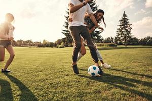Playful friends. Group of young people in casual wear running while playing soccer outdoors photo