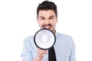 Everybody listen to me  Furious young man in shirt and tie holding megaphone and shouting while standing against white background photo