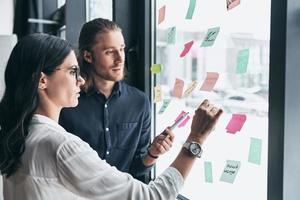 otra buena idea dos jóvenes colegas con ropa informal inteligente usando notas adhesivas en la ventana mientras trabajan juntos en la oficina foto